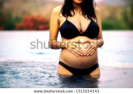 Asian pregnant woman with big belly  made hand in heart shape at the stomach, Relax and exercise and yoga at swimming pool, Water Yoga.