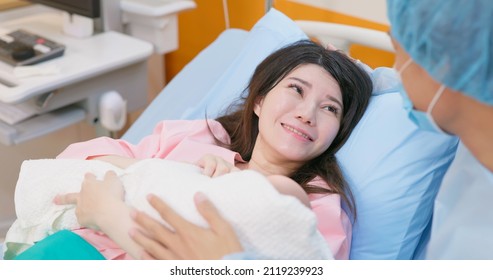 Asian Pregnant Woman In Delivery Room Is Giving Birth Successfully While Husband Accompany Her And She Hugging Their Baby In Hospital