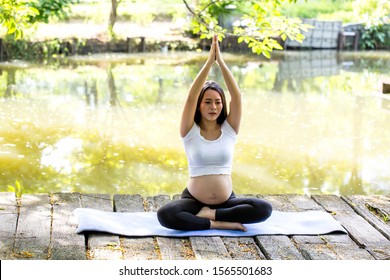 Asian Pregnant woman doing stretching and yoga.Happy Young pregnant woman doing yoga in the park, pregnancy, yoga, sports and healthcare and healthy lifestyle ,Motherhood, pregnancy, yoga concept