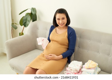 Asian pregnant woman expectant mother prepares clothing items for the newborn baby - Powered by Shutterstock