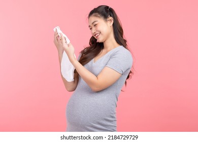 Asian Pregnant Woman Holding Baby Cloth For Baby Newborn Isolated On Pink Background. Pregnant Woman Packing Baby Stuff Ready For The Maternity Hospital. Pregnancy Proud Prepare For Newborn Concept