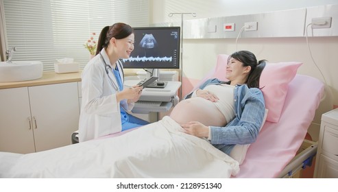 Asian Pregnant Woman Lying In Hospital Ward Has Uterus Utltrasonographic Diagnosis - Female Doctor Shows Picture On Computer And Takes Notes By Digital Tablet