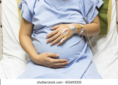 Asian Pregnant Woman patient is on drip receiving a saline solution on bed VIP room at hospital, selective focus.