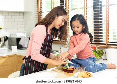 Asian Preschool Kid Person Make Cake Cooking In Kitchen, Mother Prepare Decoration Pretty With Fun Educate On Cupcake For Birthday Sister. Cream Mess All Over Hair Face Mouth, Feel Happy, Copy Space