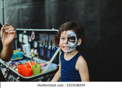 Asian Preschooler Doing Skeleton Face Paint In The Outdoor Ready For Carnival. Halloween Party In Outdoors. Long Haired Kid With Blue Shirt. Cheerful Child Ready For Festival. Activity For Children.