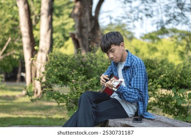 Asian preteen boy in blue plaid shirt sitting on plank and practicing ukulele lonely and seriously, soft focus, cocept for lifestyle of young people. - Powered by Shutterstock