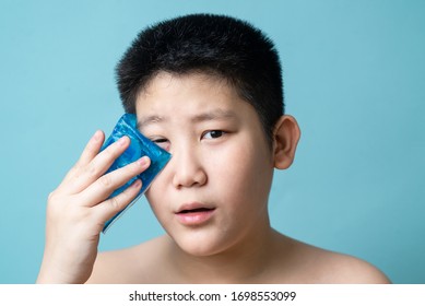 Asian Preteen Boy Using Cold Compress Gel On Bruises Face On Blue Background.