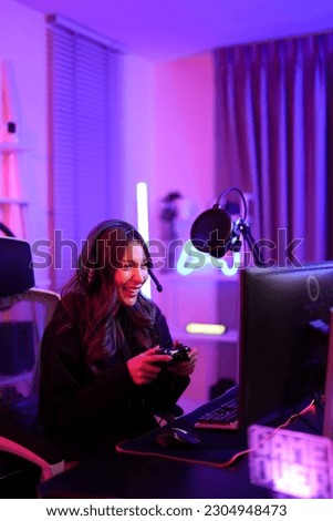 Asian pretty gamer girl use joystick when playing video game on computer screen while sitting ergonomic chair in entertainment pink neon room