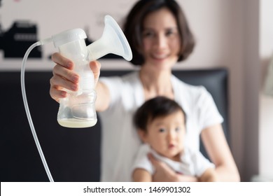 Asian pretty mother holding breast pump milk on the bed in bedroom.  Mother hugging her little cute baby in arm and feeling happy expression on face. Breast Pumping milk concept.