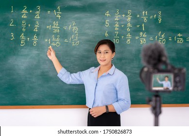 Asian Primary Teacher Tutor Explaining Math In Blackboard Giving Remote School Class Online Lesson Teaching Looking At Camera In Classroom By E-learning Livestream  Video Conference.
