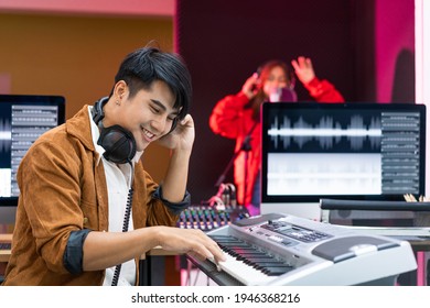 Asian producer standing by sound mixing console. Happy male music composer artist with a woman singer background   - Powered by Shutterstock