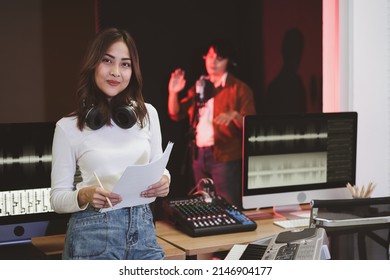 Asian producer woman in white shirt standing by sound mixing console. Happy female music composer artist with a man singer background  
 - Shutterstock ID 2146904177