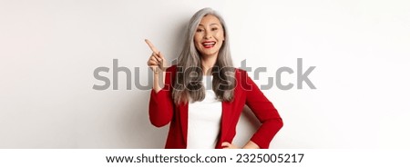 Asian professional businesswoman showing logo, smiling and pointing finger upper right corner, standing over white background.