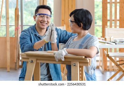 Asian professional carpenter engineer dad teaching young boy son in jeans outfit with gloves safety goggles  in home housing building construction site. - Powered by Shutterstock