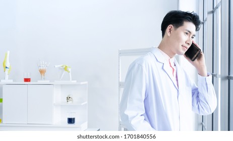 Asian Professional Doctor Young Man Make An Appointment With Friend Through Call By Mobile Phone While Standing Near Glass Window In Break Time After Check Up Diagnostic Patient In Hospital Workplace