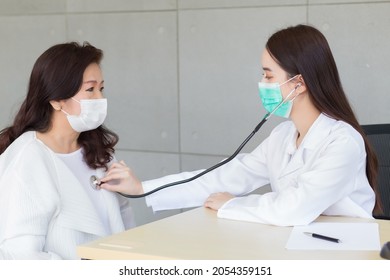 Asian Professional Female Doctor Uses Stethoscope To Check Health Of Lungs And Heart Or Diagnosis Symptom Of Woman  Elderly Patient While Both Wear Face Mask In Hospital.