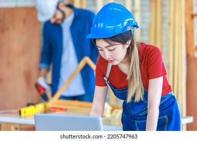 Asian Professional Female Engineer Architect Foreman Labor Worker Wears Safety Goggles And Jeans Apron Standing Smiling Using Laptop Computer Working On Wooden Table With Tools In Construction Site.