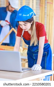 Asian Professional Female Engineer Architect Foreman Labor Worker Wears Safety Goggles And Jeans Apron Standing Smiling Using Laptop Computer Working On Wooden Table With Tools In Construction Site.