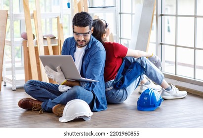 Asian Professional Female And Indian Bearded Male Engineer Architect Foreman Labor Worker Wear Safety Goggles And Gloves Sitting On Floor Smiling Working With Laptop Computer Discussing Together.