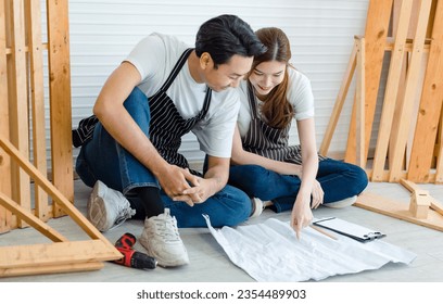 Asian professional male and female carpenter worker lover couple colleague in apron sitting on floor smiling discussing talking looking at  blueprint information data in home decoration workshop. - Powered by Shutterstock