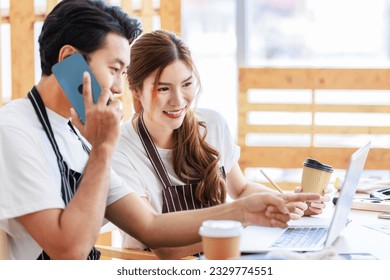 Asian professional male and female lover couple carpenter worker in apron looking pointing blueprint planning via laptop computer on wooden table with equipment in home decoration building workshop. - Shutterstock ID 2329774551