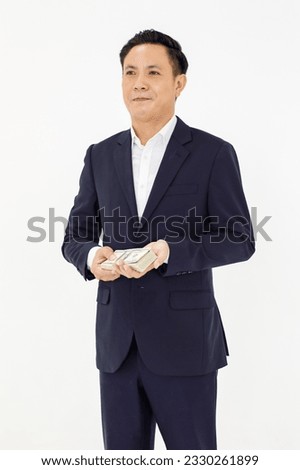 Asian professional successful rich wealthy millionaire male businessman entrepreneur accountant in formal business suit standing holding stack of hundred dollar banknote currency on white background.