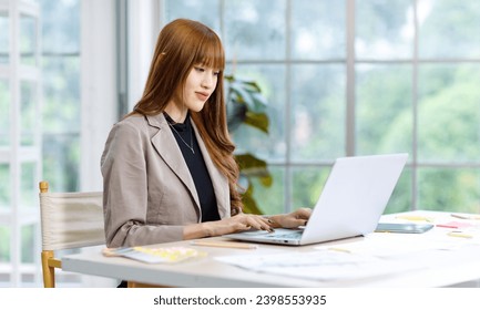 Asian professional successful young female businesswoman creative graphic designer employee in casual fashionable suit blazer outfit sitting working using typing laptop computer at office workstation. - Powered by Shutterstock