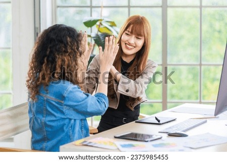 Asian professional successful young female businesswoman creative graphic designer in casual outfit sitting holding fists up celebrating job deal done acheivement with colleague pointing screen.