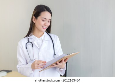 Asian Professional Woman Doctor Examine Report Document Of Patient To Plan The Next Treatment. She Look At The Clipboard In Her Hand While Working At Hospital.