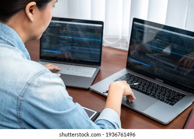 Asian programmer woman looking on multiple laptop screen and holding pen pointing while working to writing coding database and development website or applications in software development office