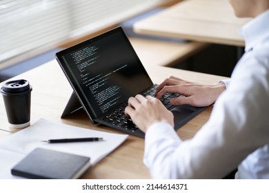 Asian programmer writing code on a laptop - Shutterstock ID 2144614371