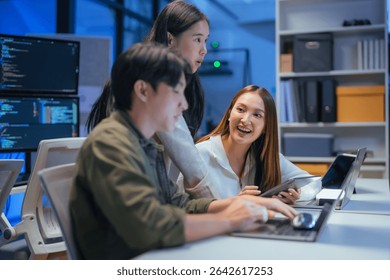 Asian programmers collaborating on software development at night, focused on writing code across multiple monitors in a tech office environment Programmers Collaborating on Software Development