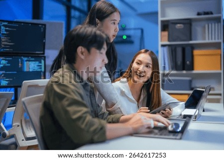 Asian programmers collaborating on software development at night, focused on writing code across multiple monitors in a tech office environment Programmers Collaborating on Software Development