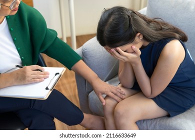 Asian psychologist doctor consults psychotherapy session with young depressed woman. Psychology and mental therapy concept. - Shutterstock ID 2116633649