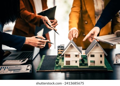 Asian real estate team engaged in a discussion, with two men and a woman focusing on a house model on a table, suggesting a planning or sales meeting. - Powered by Shutterstock