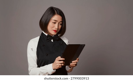 Asian restaurant server checking all table reservations on tablet, browsing through clients information on website, waitress looking at online webpages to see availability.