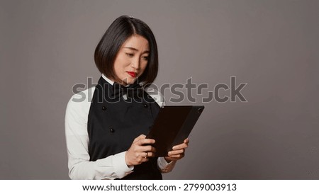 Asian restaurant server checking all table reservations on tablet, browsing through clients information on website, waitress looking at online webpages to see availability.