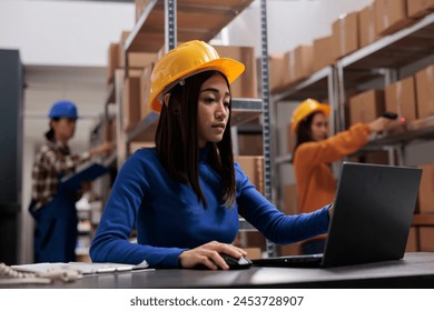 Asian retail storehouse employee analyzing orders checklist on laptop while working in storage room. Warehouse manager supervising inventory management while using computer - Powered by Shutterstock