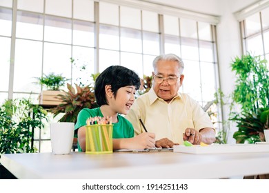 Asian Retirement Grandfather And His Grandson Spending Quality Time Together Insulated At Home. Enjoy Drawing With Colored Pencils. Family Bonding Between Old And Young. Concept Of Quarantine.