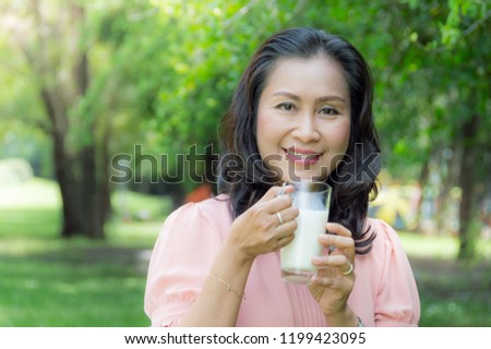 Asian retirement women are drinking milk for good health with blurred soft green nature background To health concept.