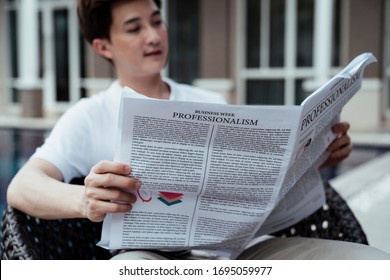 Asian Rich Guy Businessman Reading News Paper At Resort Sitting On A Chair Near Swimming Pool.