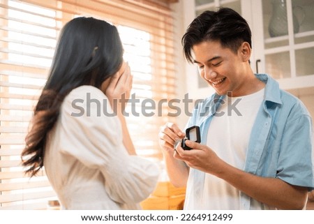 Asian romantic man making surprise proposal of marriage to girlfriend. Attractive young male and proposing to beautiful happy woman, with wedding ring enjoying surprise engagement in kitchen at home. Foto stock © 