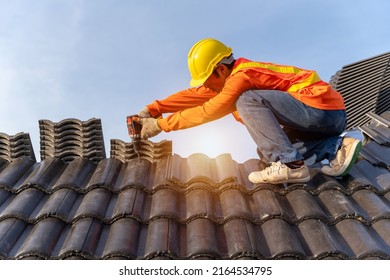 Asian Roofer Working On Roof Structure Of Building On Construction Site,Roofer Using Air Or Pneumatic Nail Gun And Installing Concrete Roof Tiles On Top New Roof.