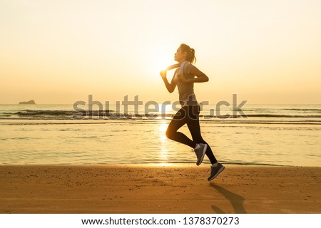 Asian runner good shape woman running on beach in sunset light with wave and sun in background. Concept in workout for good health and heathcare of modern people.