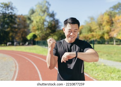 Asian running in the stadium sunny day man looks at the smartwatch and is satisfied with the result of the training, the runner in sportswear holds his hand up in a gesture of triumph and victory. - Powered by Shutterstock