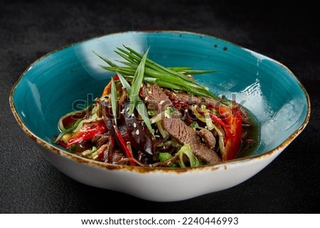 Asian salad with beef and vegetables in ceramic bowl on dark concrete background. Salad with beef fillet, muer mushrooms and green onion in chinese cuisine style. Asian menu in minimal style on black