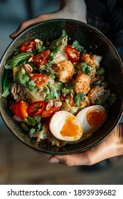 Asian salad in the woman's hands. Aisan salad with eggs, fresh greens, tomatoes, red peppers, nuts and prawns,