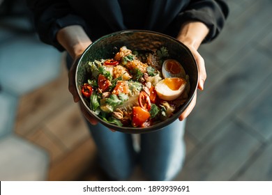Asian salad in the woman's hands. Aisan salad with eggs, fresh greens, tomatoes, red peppers, nuts and prawns,