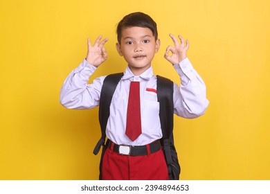 Asian school boy in uniform showing ok sign over yellow background
