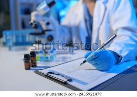 Asian scientist looking at a microscopic sample of experimental cyan is doing an in vitro vaccine experiment in a science lab. medical research concept.